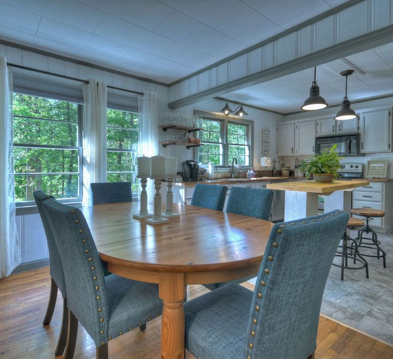 A dining room table with blue chairs and a large kitchen in the background.